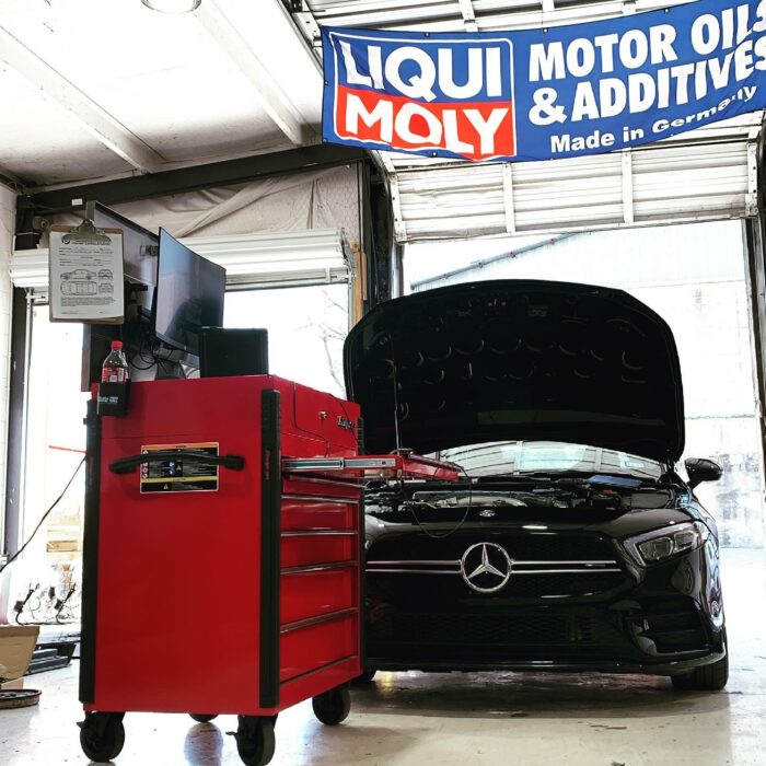 A Mercedes-Benz with its hood open in a garage getting tuned